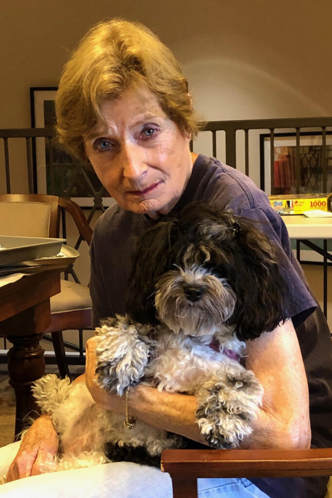 A photograph of Mary Fletcher holding her dog in her lap as she sits in a chair.