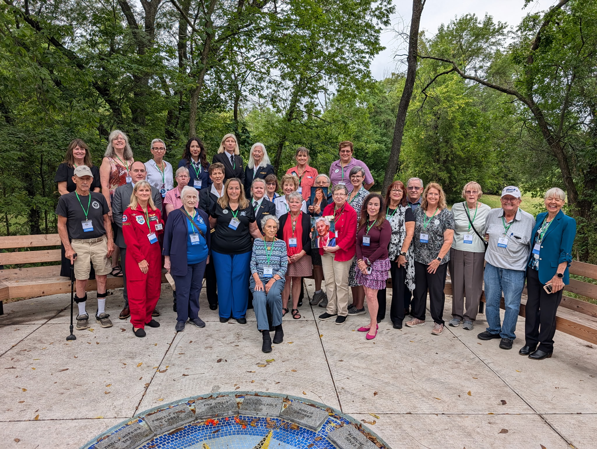 Attendees of the Forest of Friendship Celebration line up outside for a photo around a central logo floor inlay