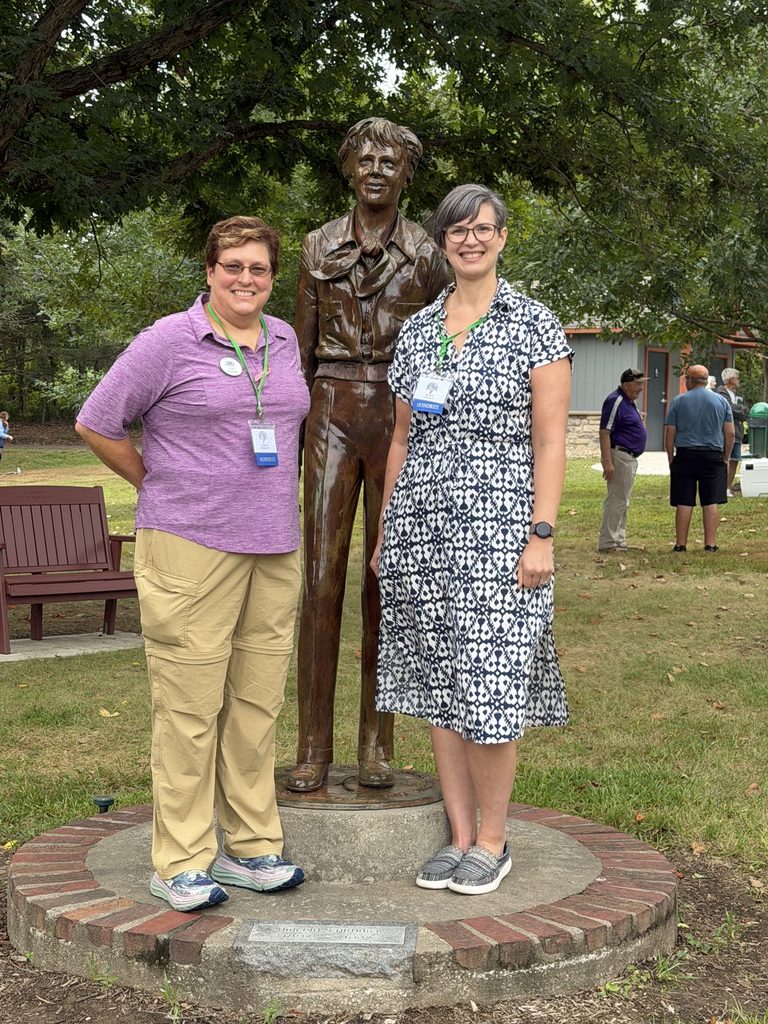 Mandi Hill and Lois Horne stand in front of a bronze statue of Amelia Earhart.