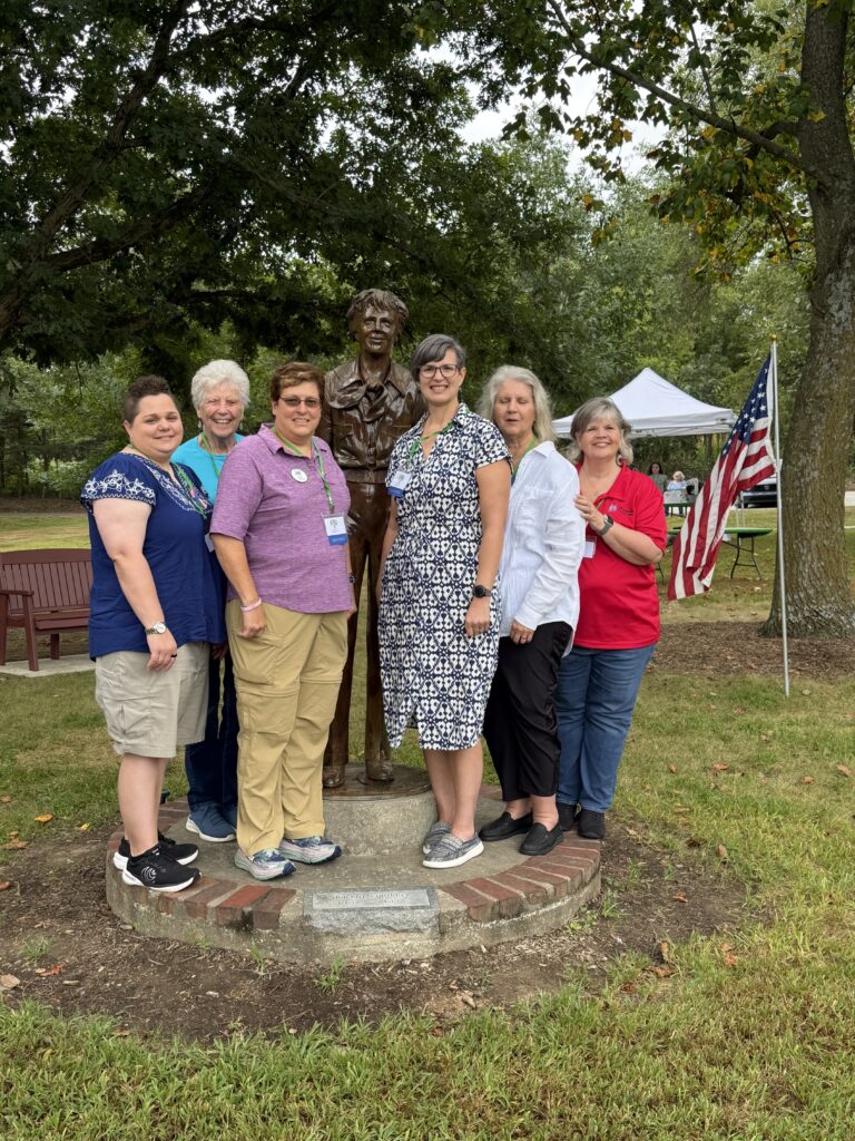 Mandi Hill and Lois Horne stand together with other members of their Memphis Chapter, who nominated the inductees, around a bronze statue of Amelia Earhart.