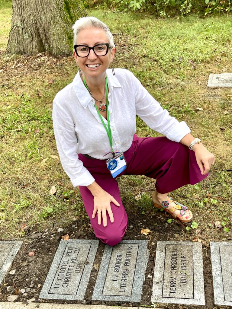 Liz Booker kneels by her plaque in the Forest of Friendship, located between fellow 99s members Terry Carbonell and Lt Col (ret) Christine Kelley.