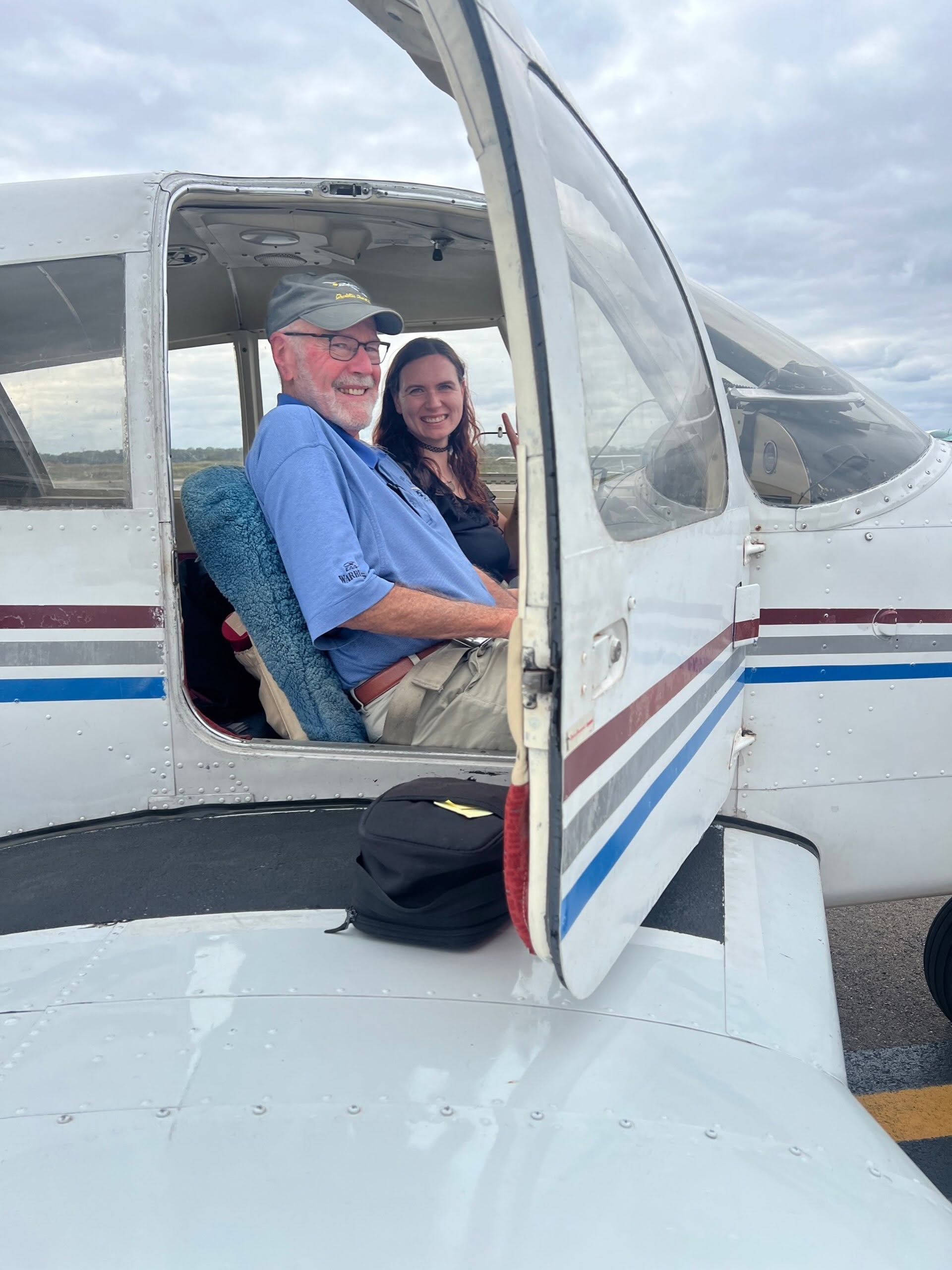 a woman and man sit in the cockpit of a lowing aircraft and smile at the camera